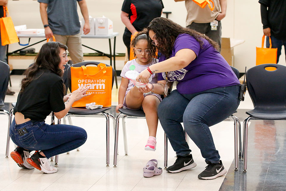 A woman helps a little girl put her new shoes on, while another woman looks on, smiling
