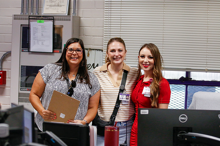 Three women smile behind the front desk in the school office