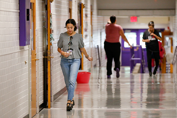 A woman in a gray shirt and jeans walks down the hallway