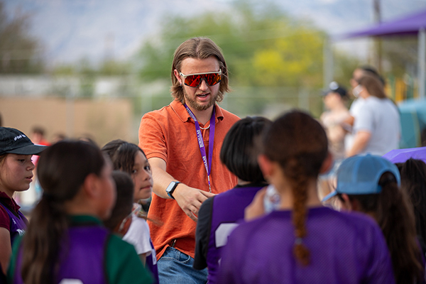 A man in an orange shirt and sunglasses talks to the kickball team