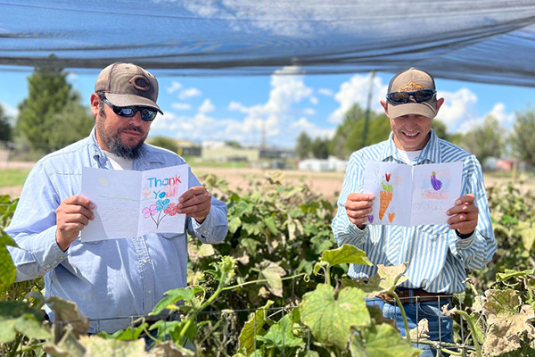 Two farmers standing in a field reading cards hand-drawn by students