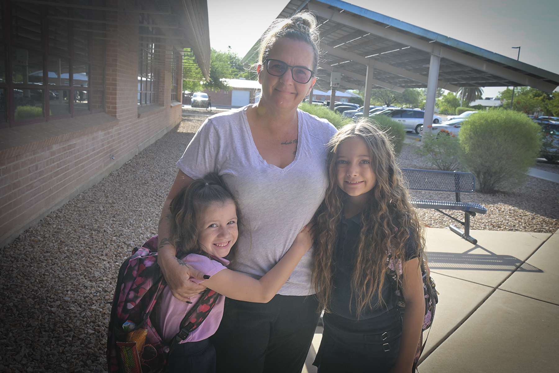 A mom and her two daughters smile for a photo outside the school