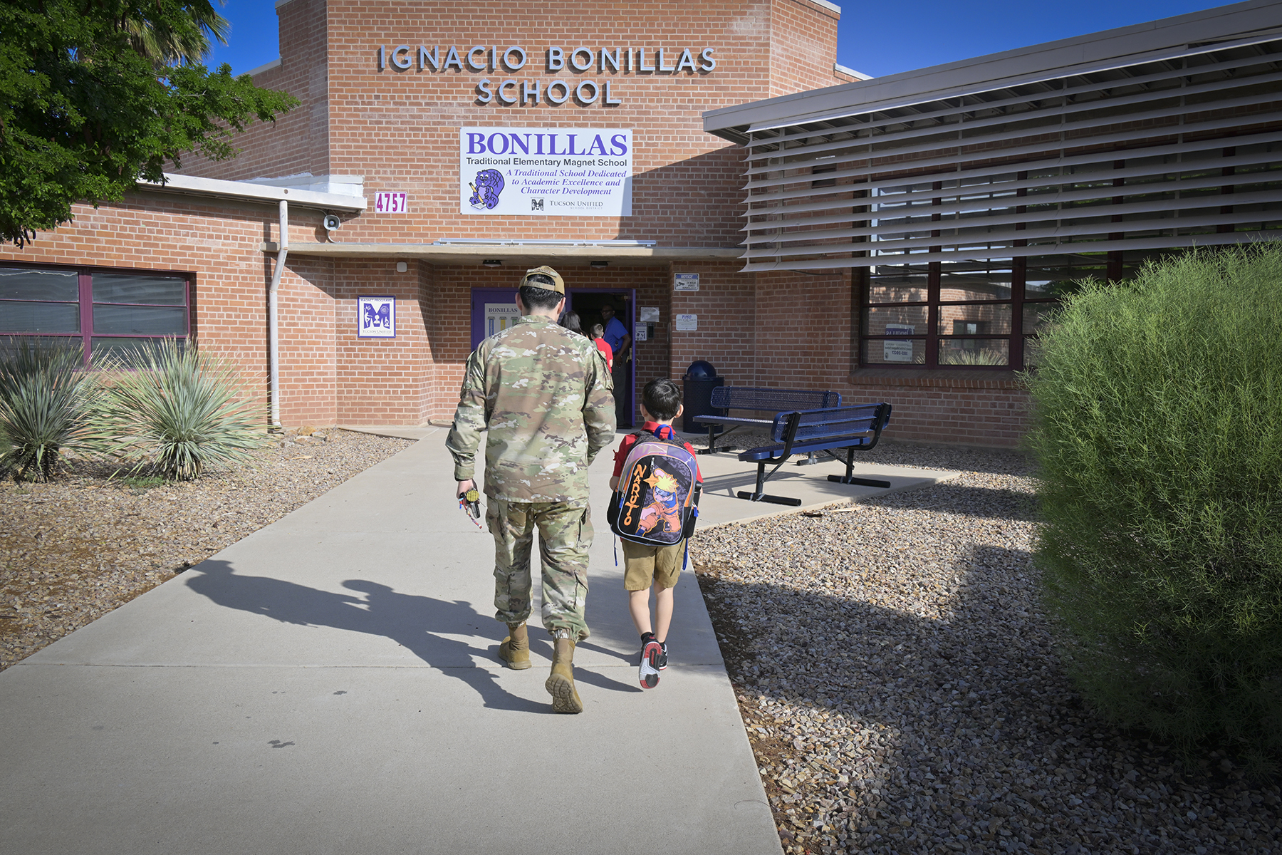 A mom in military fatigues walks her young son into school