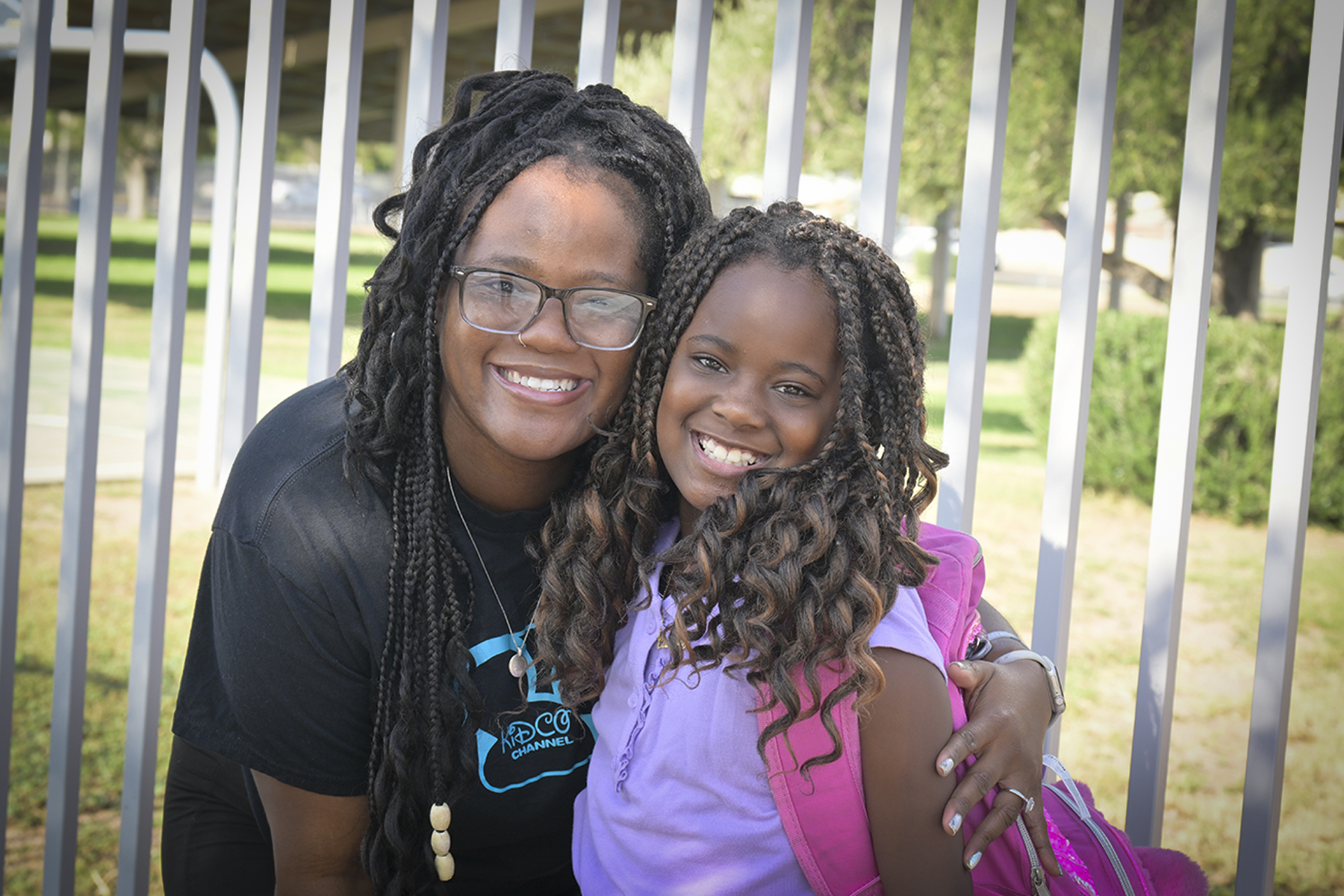 A mom and her daughter smile in front of the school fence