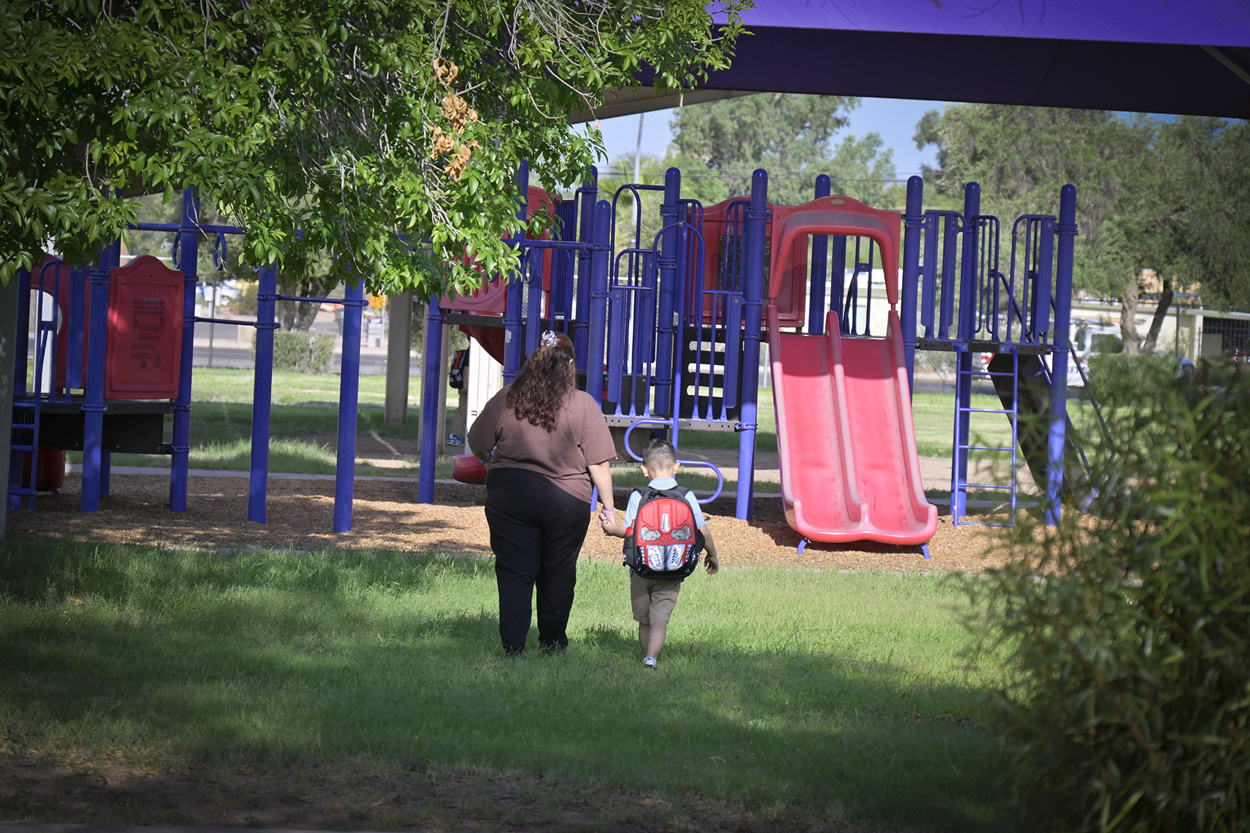 A mom and her young son walk towards the playgroun