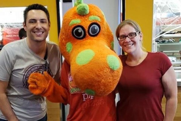 Two Adults Smiling with An Orange Dinosaur 